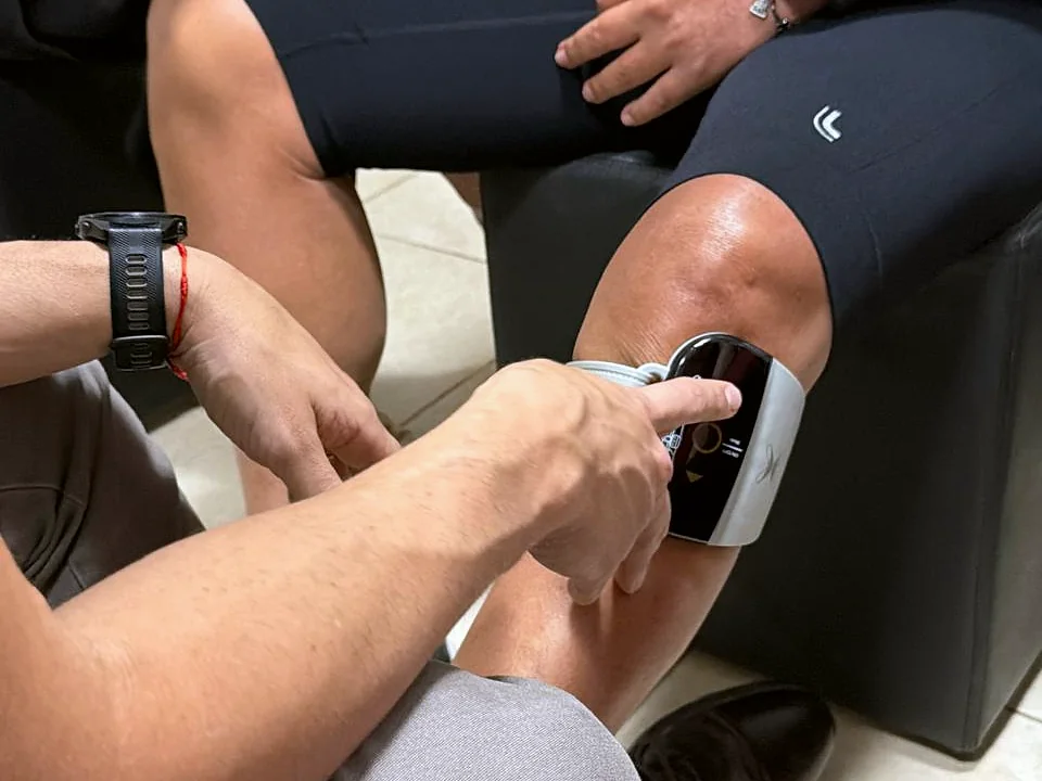 Profissional ajustando o G4 na perna de um paciente sentado, tocando a interface do aparelho